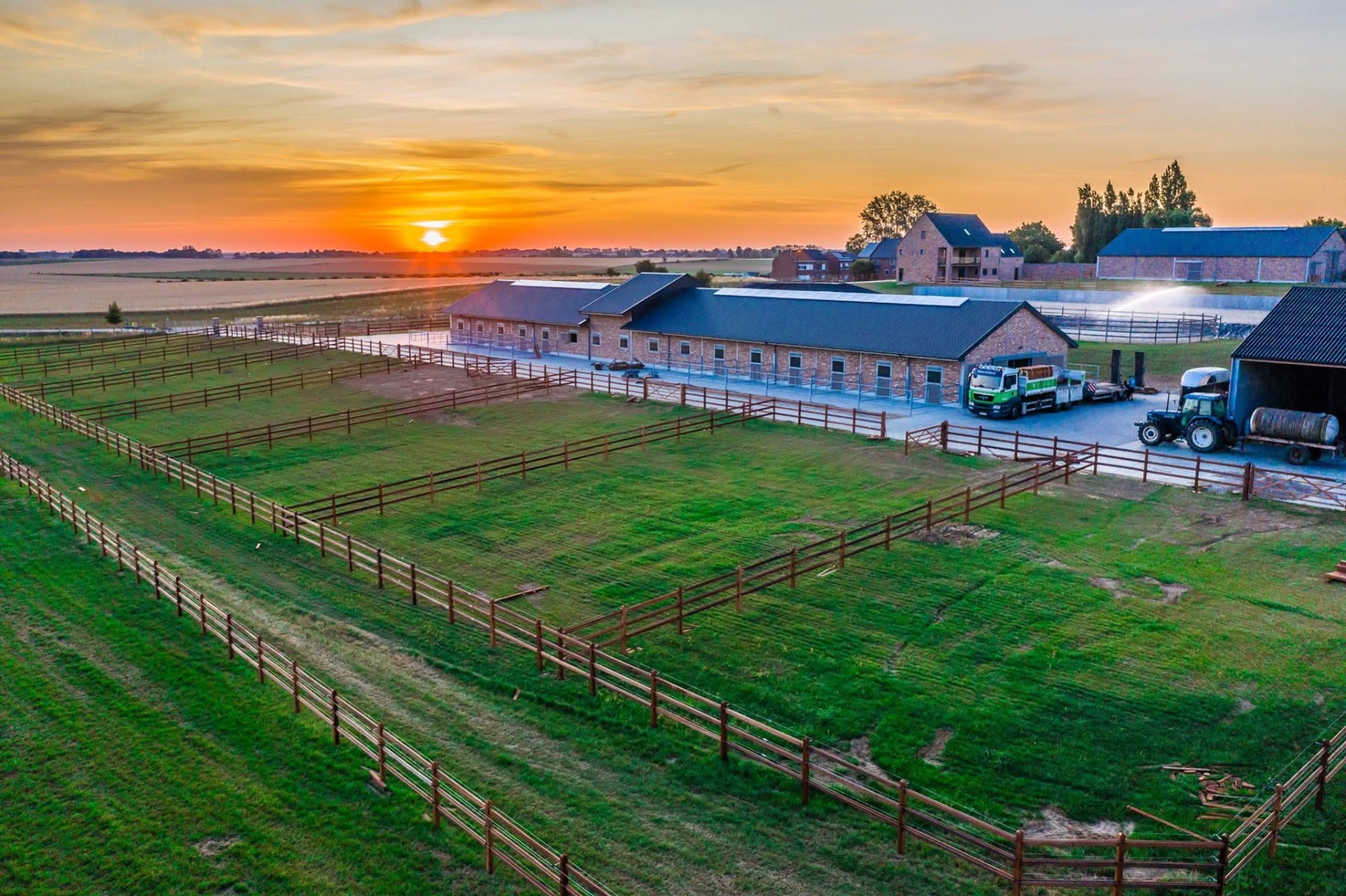 Paddocks with wooden fencing by a stable at sunset